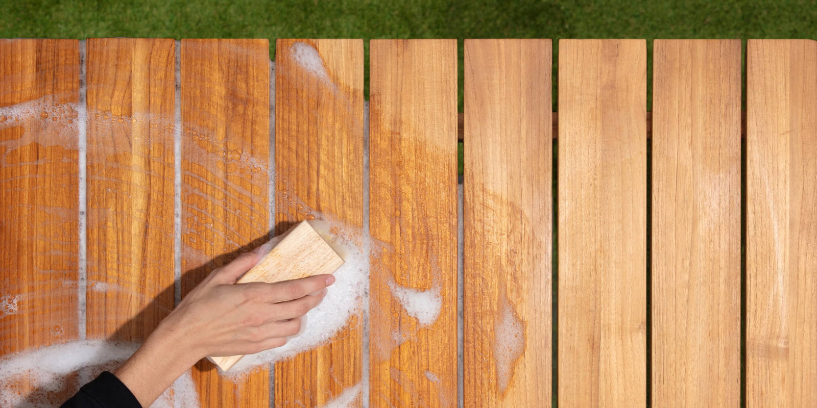 Woman's hand with bristled brush cleaning teak table with soap