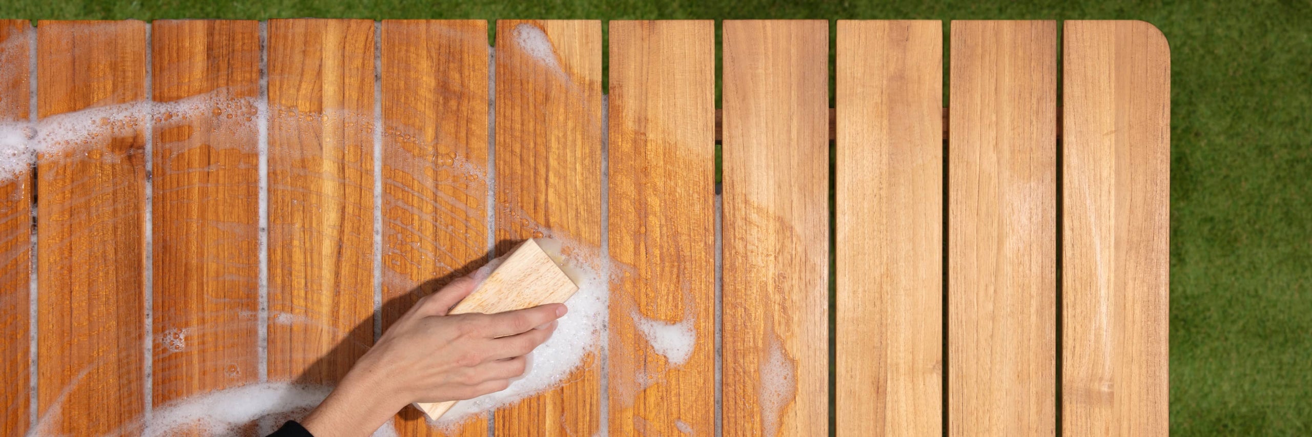 Woman's hand with bristled brush cleaning teak table with soap