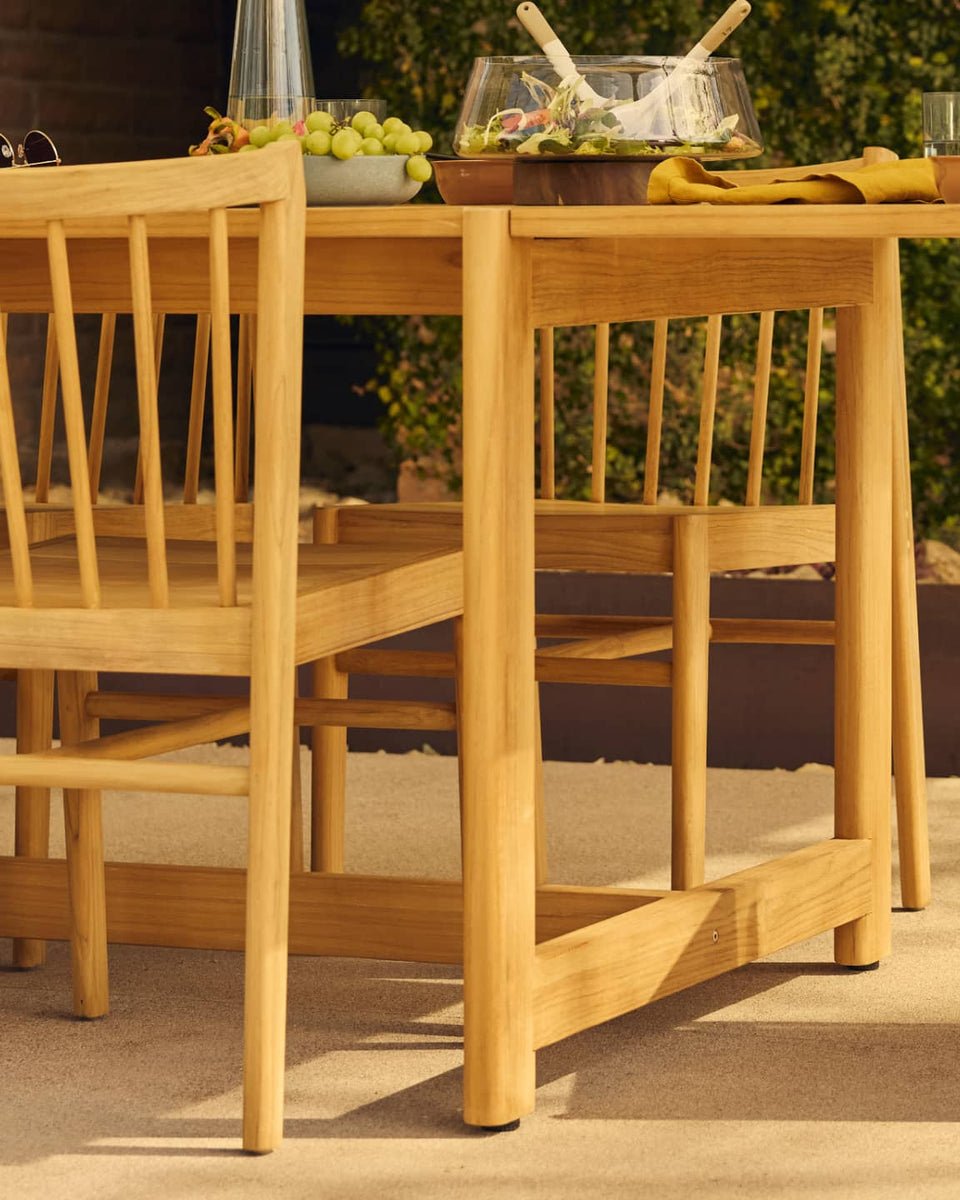 teak outdoor dining table with woman's body in motion in foreground