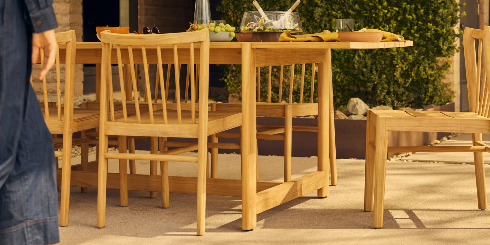 teak outdoor dining table with woman's body in motion in foreground