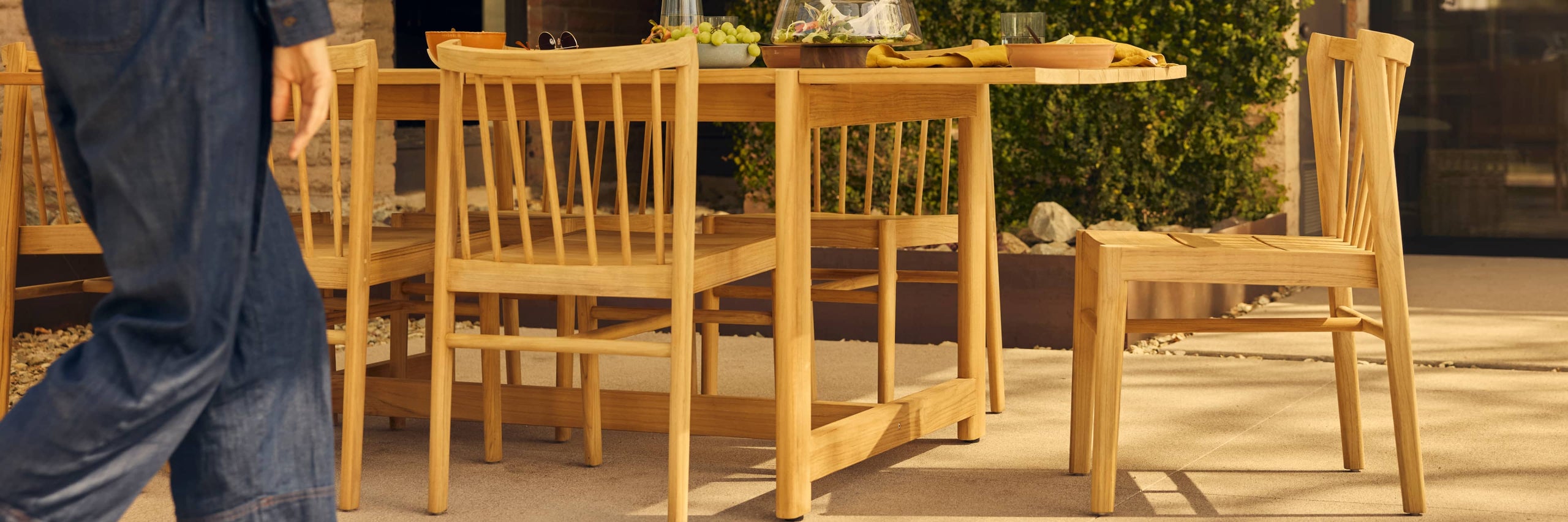 teak outdoor dining table with woman's body in motion in foreground