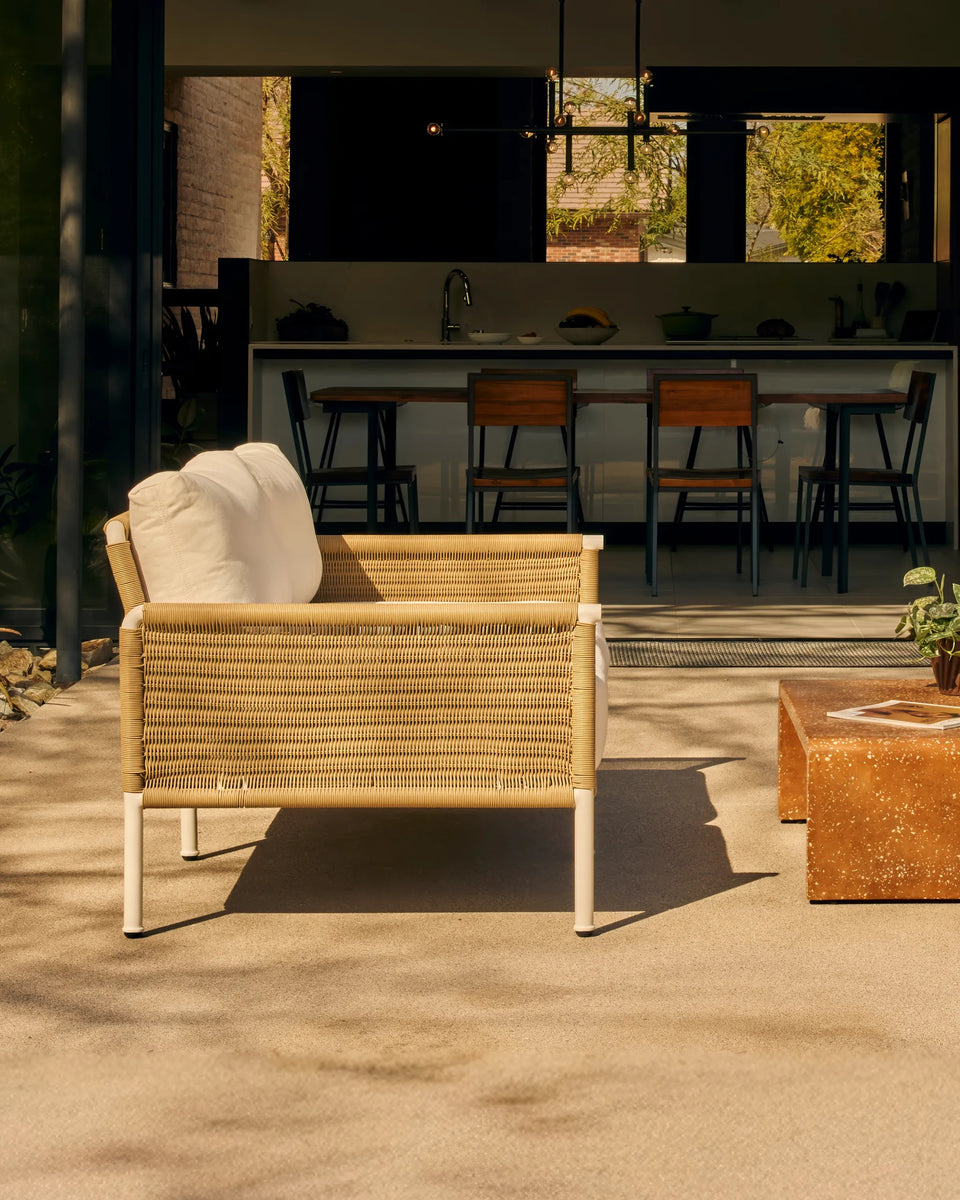 Rattan outdoor sofa with white cushions in a sunny backyard