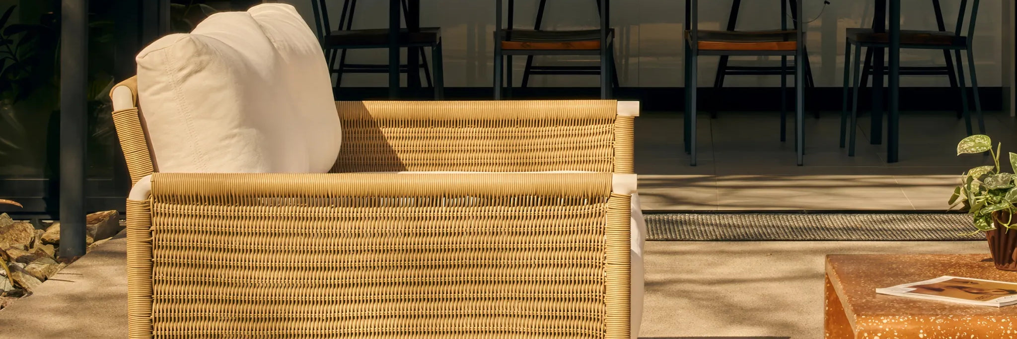 Rattan outdoor sofa with white cushions in a sunny backyard
