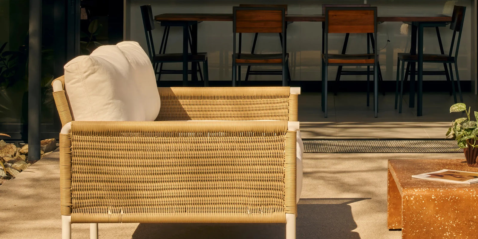 Rattan outdoor sofa with white cushions in a sunny backyard