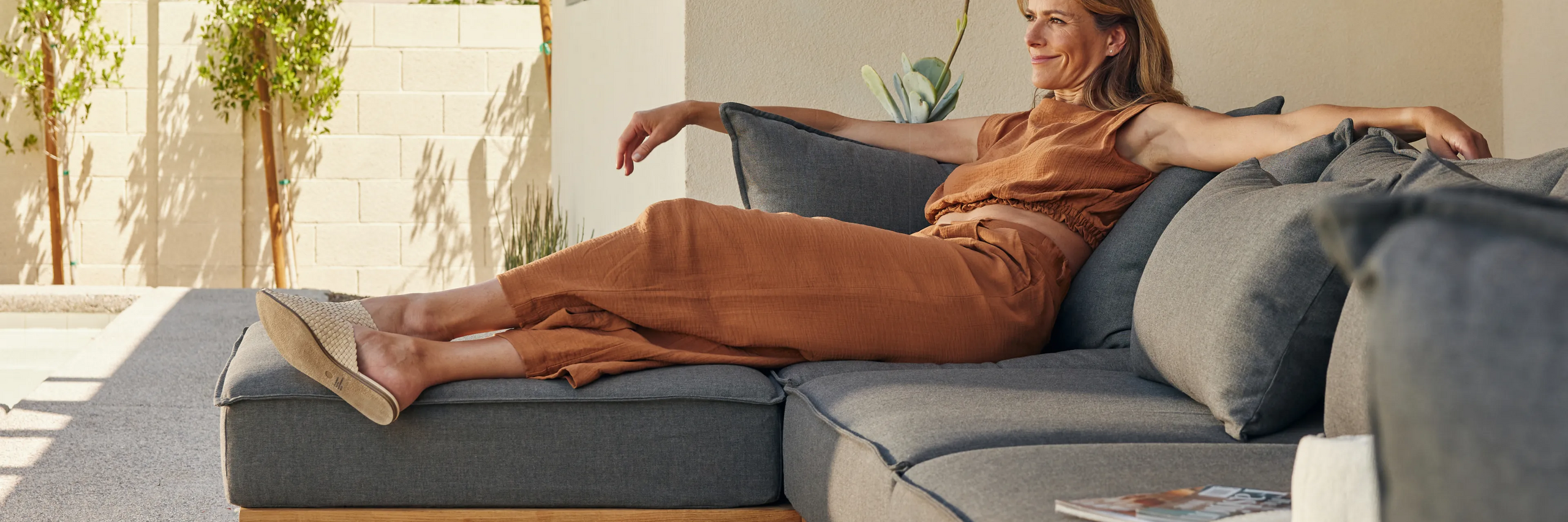 Woman lounging outside on a grey upholstered teak outdoor sectional