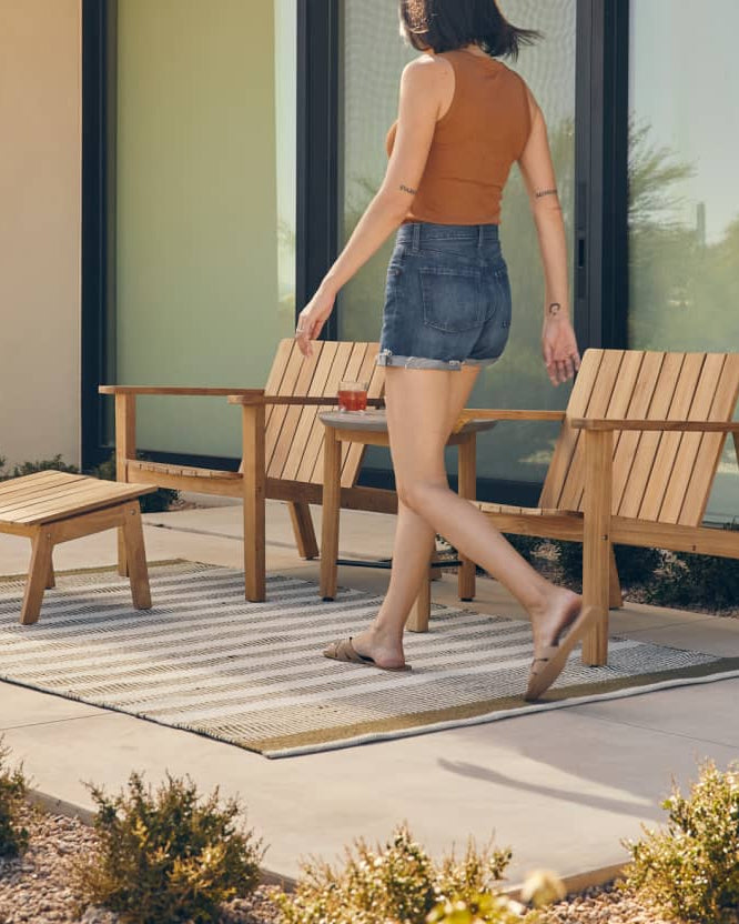 Woman in a backyard walking past two teak adirondack chairs
