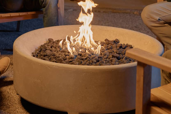 Neighbor round concrete fire pit table in a backyard surrounded by friends sat in teak Adirondack chairs