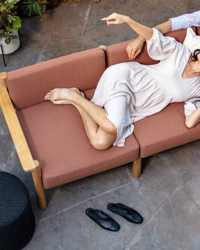 Couple comfortably laying on rust-colored outdoor sofa together