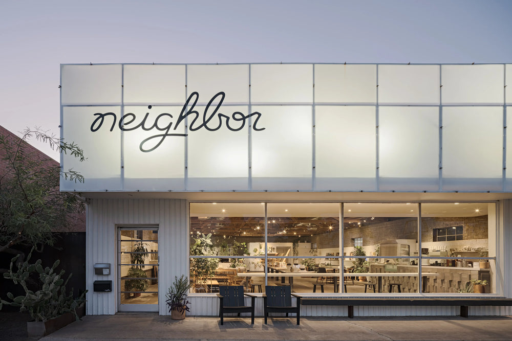 Wide exterior view of the Neighbor showroom at dusk, furniture displays visible through large windows