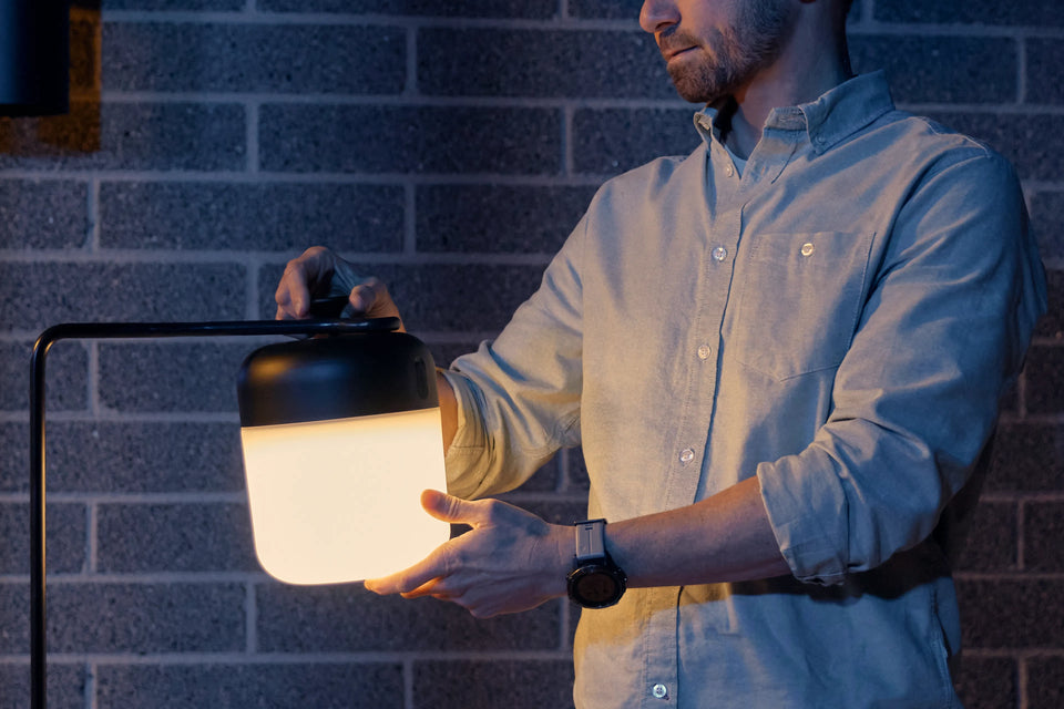 Man attaching Neighbor Acorn Lantern to the Acorn Stand against a brick exterior wall at dusk