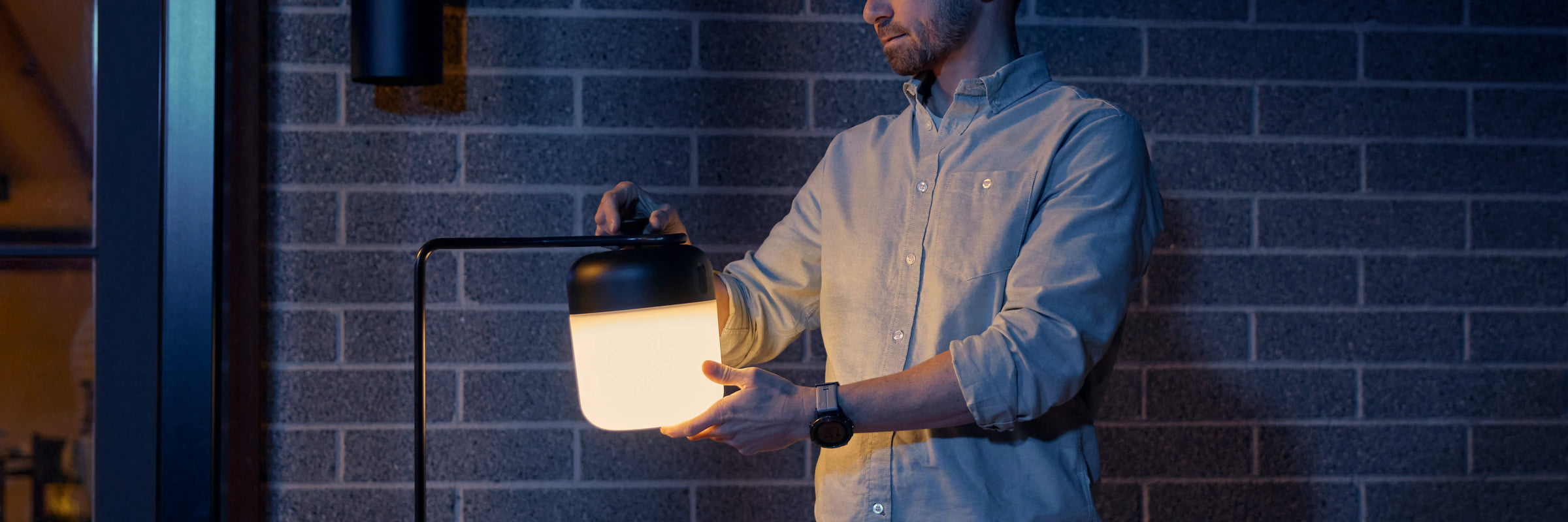 Man attaching Neighbor Acorn Lantern to the Acorn Stand against a brick exterior wall at dusk
