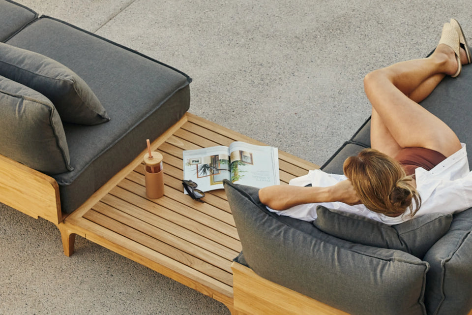 Overhead view of Neighbor Bluff Sectional with In-line Table in charcoal and teak, woman reading on travertine patio
