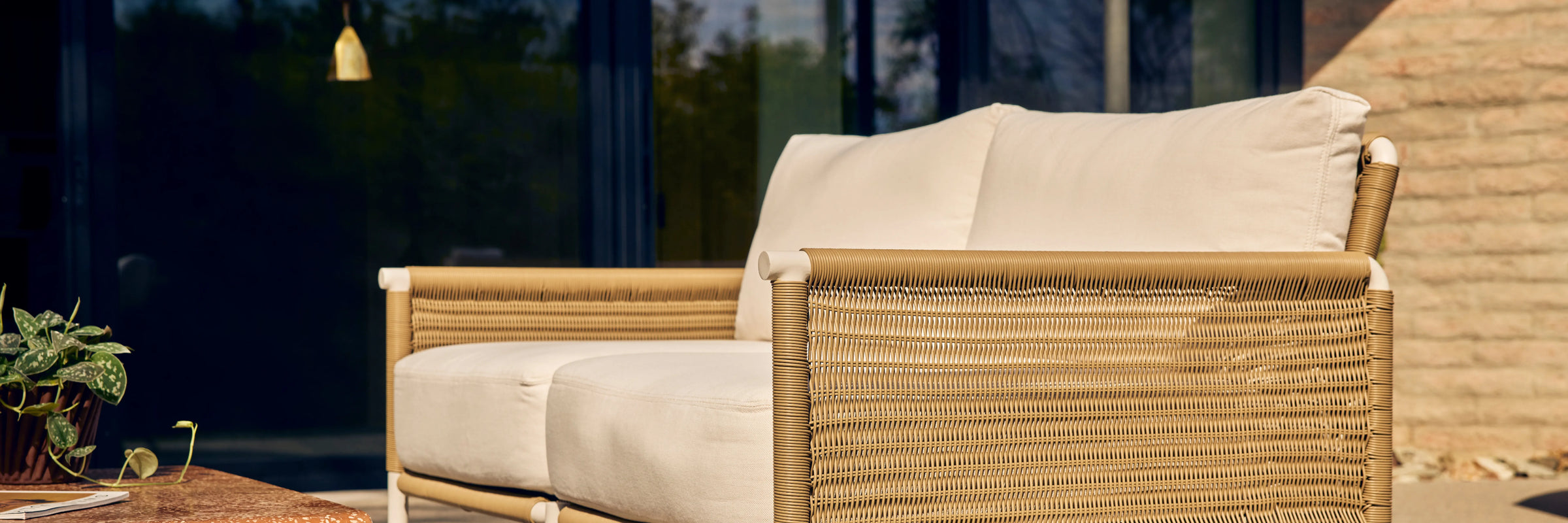 Neighbor Camber Loveseat with natural wicker frame and cream cushions on a sunlit outdoor patio