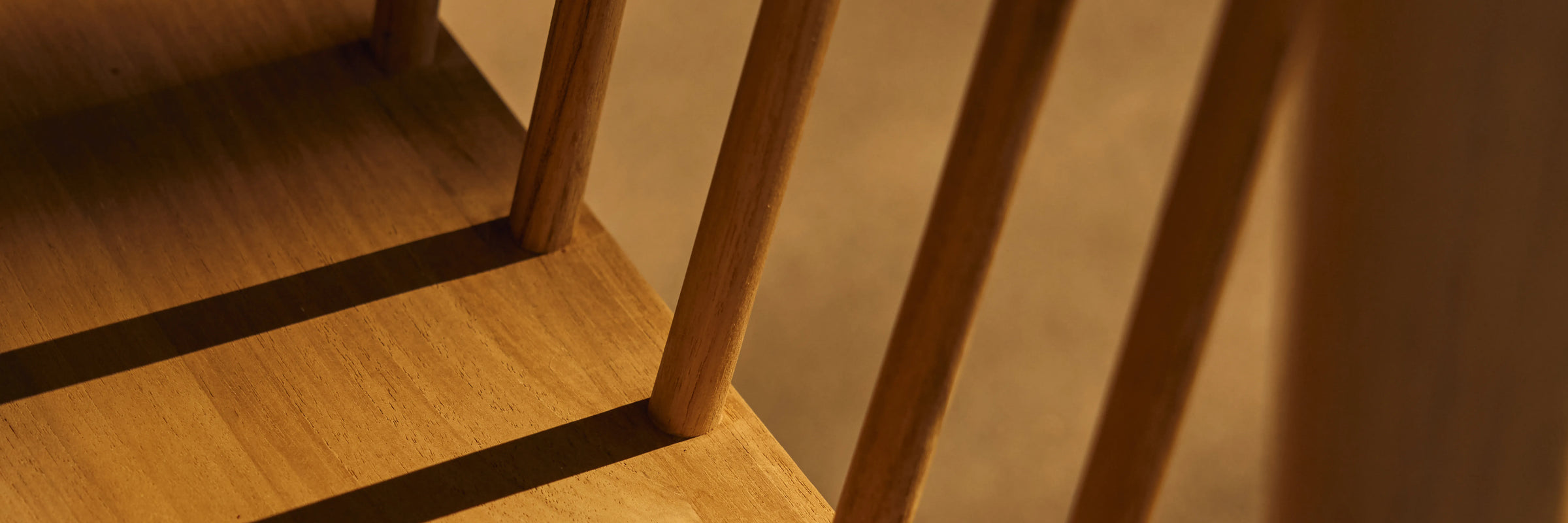 Closeup of Neighbor Felloe Dining Chair back spindles casting shadows on teak seat in raking afternoon light