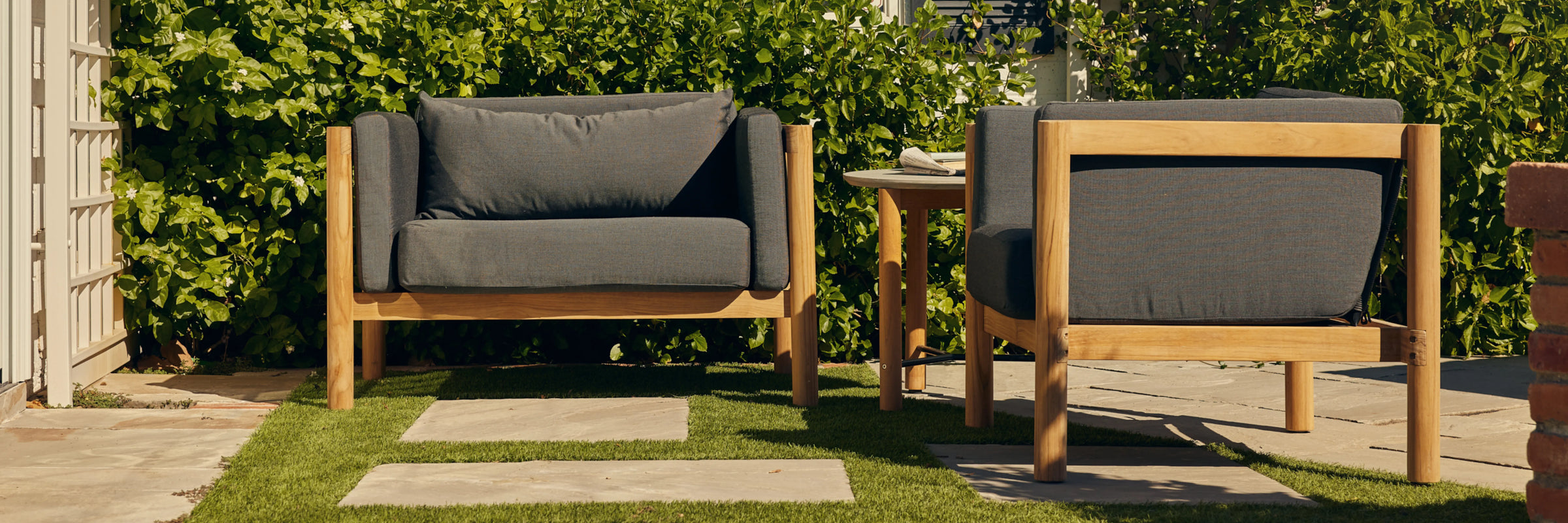 Person seated on Neighbor Haven Chair and a Half in charcoal fabric and teak frame on a sunny backyard patio