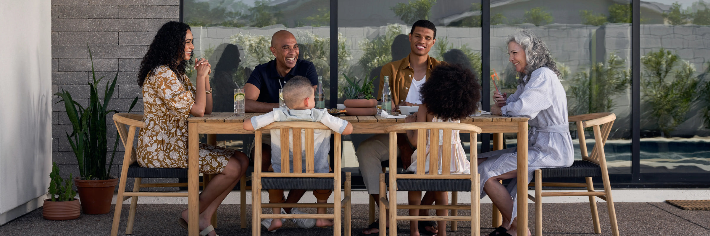 Family dining together on Neighbor Haven Dining Set with teak table and woven-seat chairs on a covered porch
