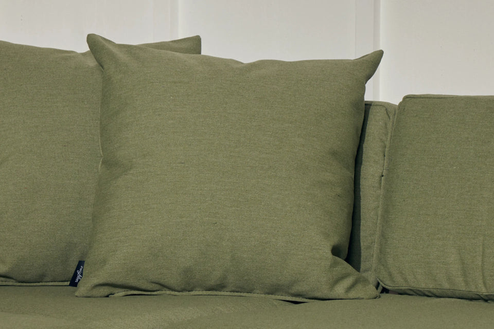 Neighbor Haven Throw Pillows in olive green stacked on a matching green outdoor sofa against a white wall