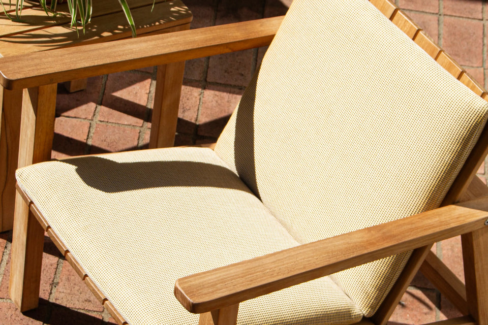 Neighbor Low Chair with cream cushion pad on teak frame on a terracotta tile patio in bright sun