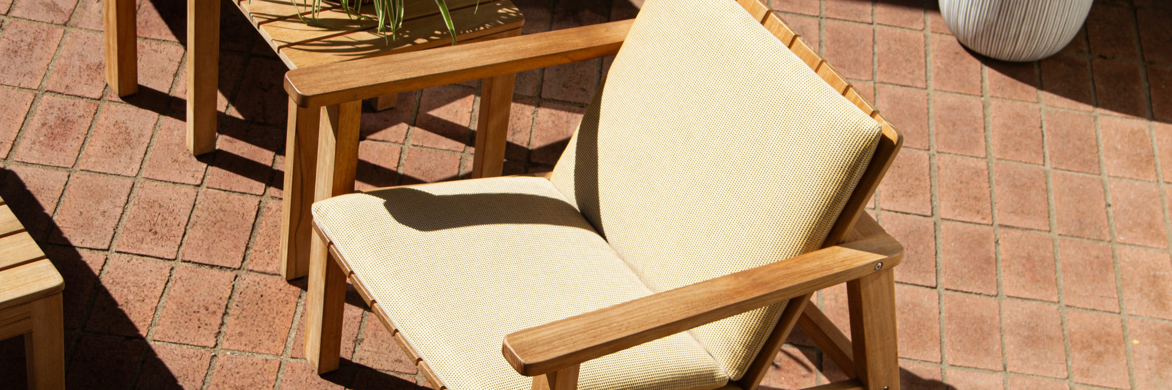 Neighbor Low Chair with cream cushion pad on teak frame on a terracotta tile patio in bright sun