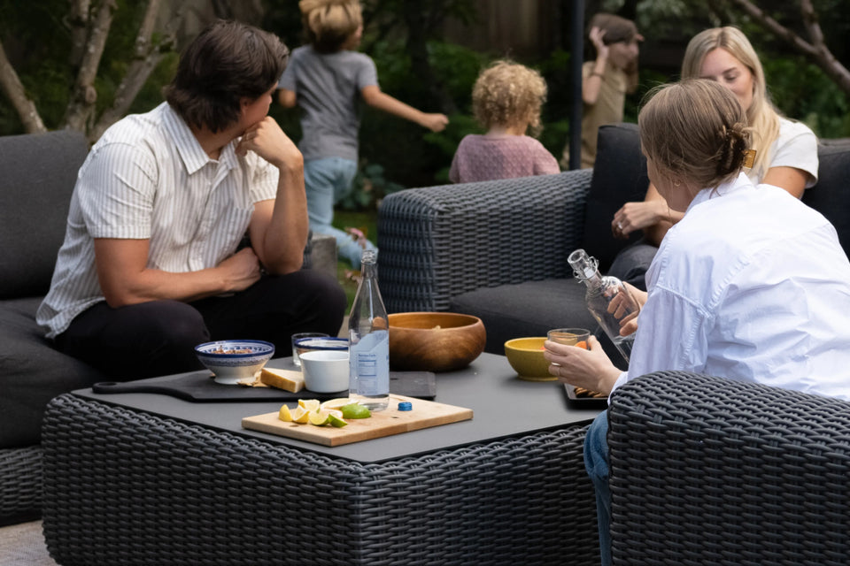 Neighbor Roundabout collection with dark wicker seating and coffee table on a stone-paved patio at dusk