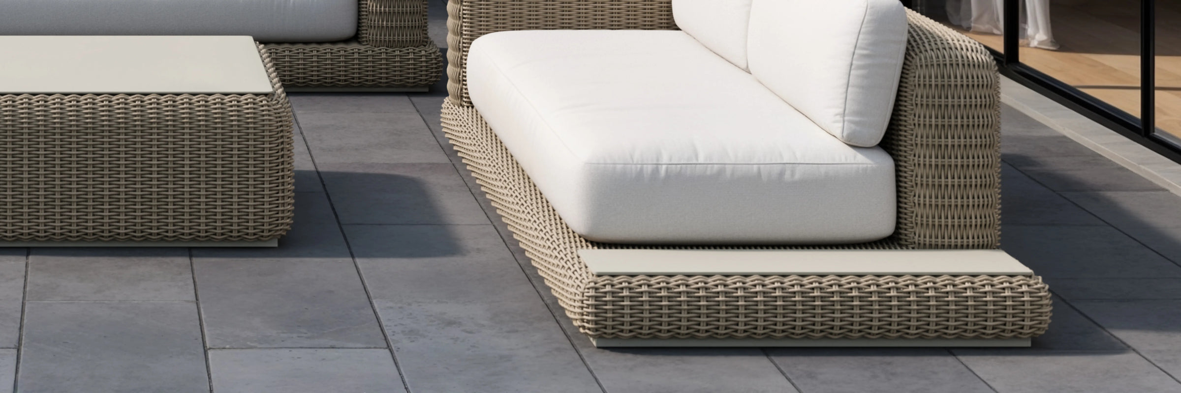 Neighbor Roundabout Sofa with Side Table in dark wicker and charcoal cushions on a stone patio with garden
