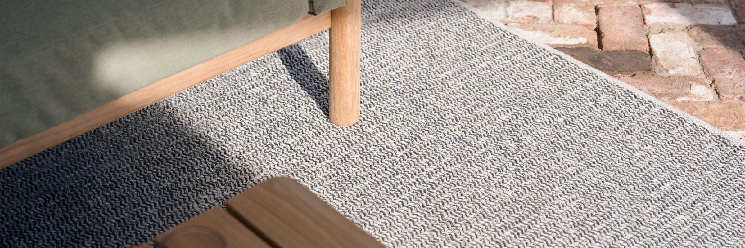 Neighbor Braid Outdoor Rug with woven stripe pattern on a patio surface, partial view showing texture and edge