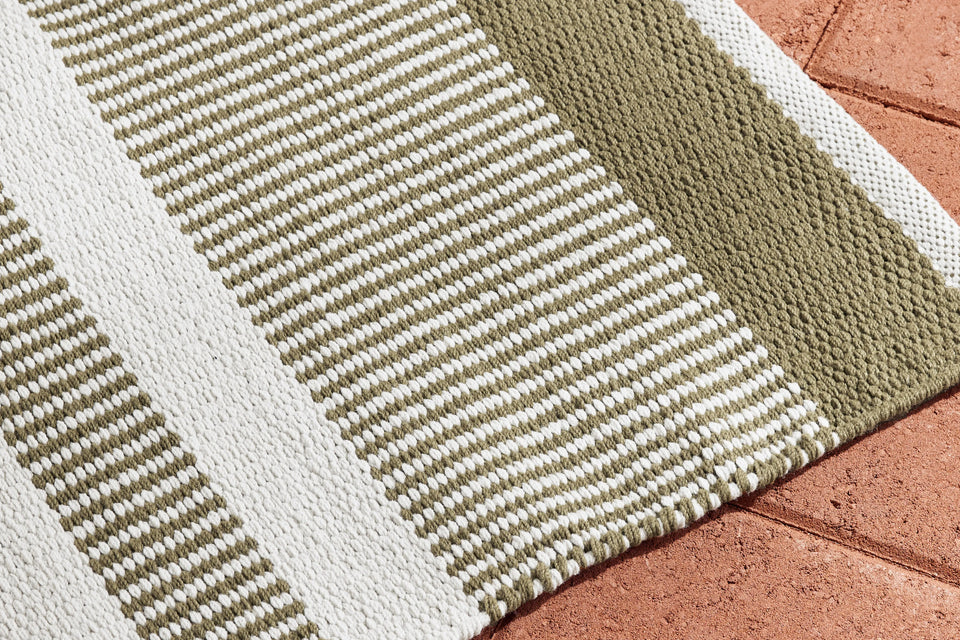Neighbor Dune Outdoor Rug with green and white stripe pattern draped on terracotta tile floor, showing texture