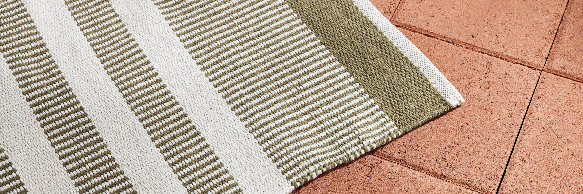 Neighbor Dune Outdoor Rug with green and white stripe pattern draped on terracotta tile floor, showing texture