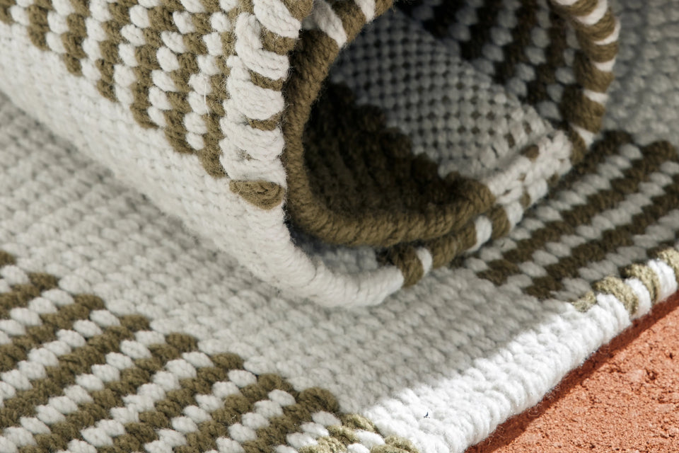 Closeup of Neighbor Dune Outdoor Rug green and white woven stripe pattern on terracotta floor