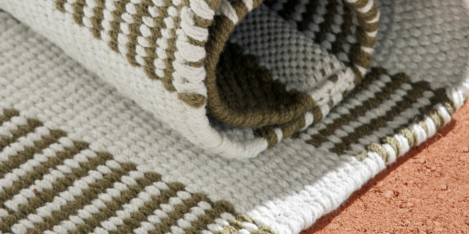 Closeup of Neighbor Dune Outdoor Rug green and white woven stripe pattern on terracotta floor