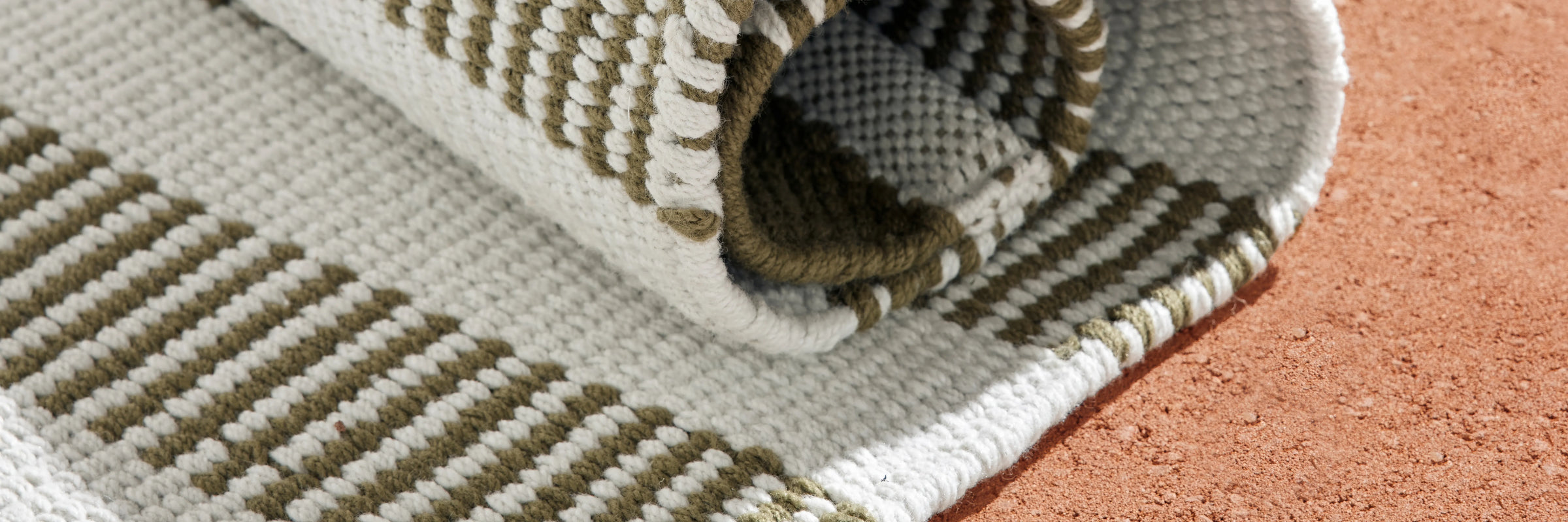 Closeup of Neighbor Dune Outdoor Rug green and white woven stripe pattern on terracotta floor