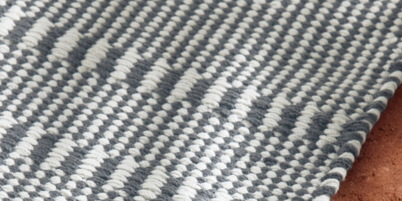 Neighbor Field Outdoor Rug with tonal woven pattern on an outdoor patio surface, partial lifestyle view