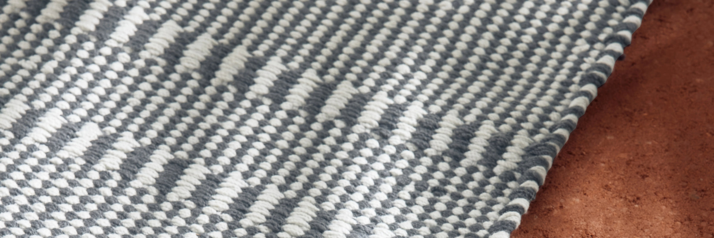 Neighbor Field Outdoor Rug with tonal woven pattern on an outdoor patio surface, partial lifestyle view