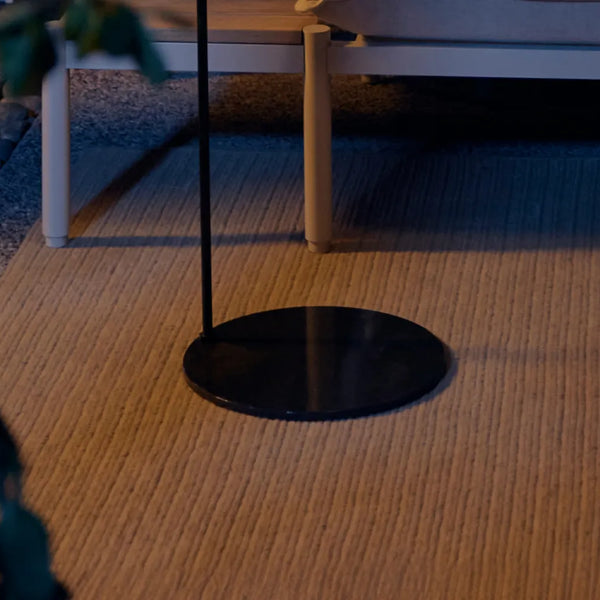 Weighted disc base of Acorn Stand on woven outdoor rug — low-angle view at dusk