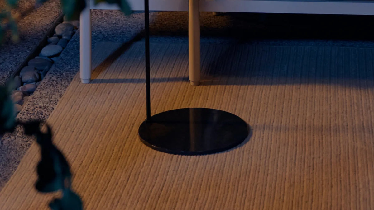 Weighted disc base of Acorn Stand on woven outdoor rug — low-angle view at dusk