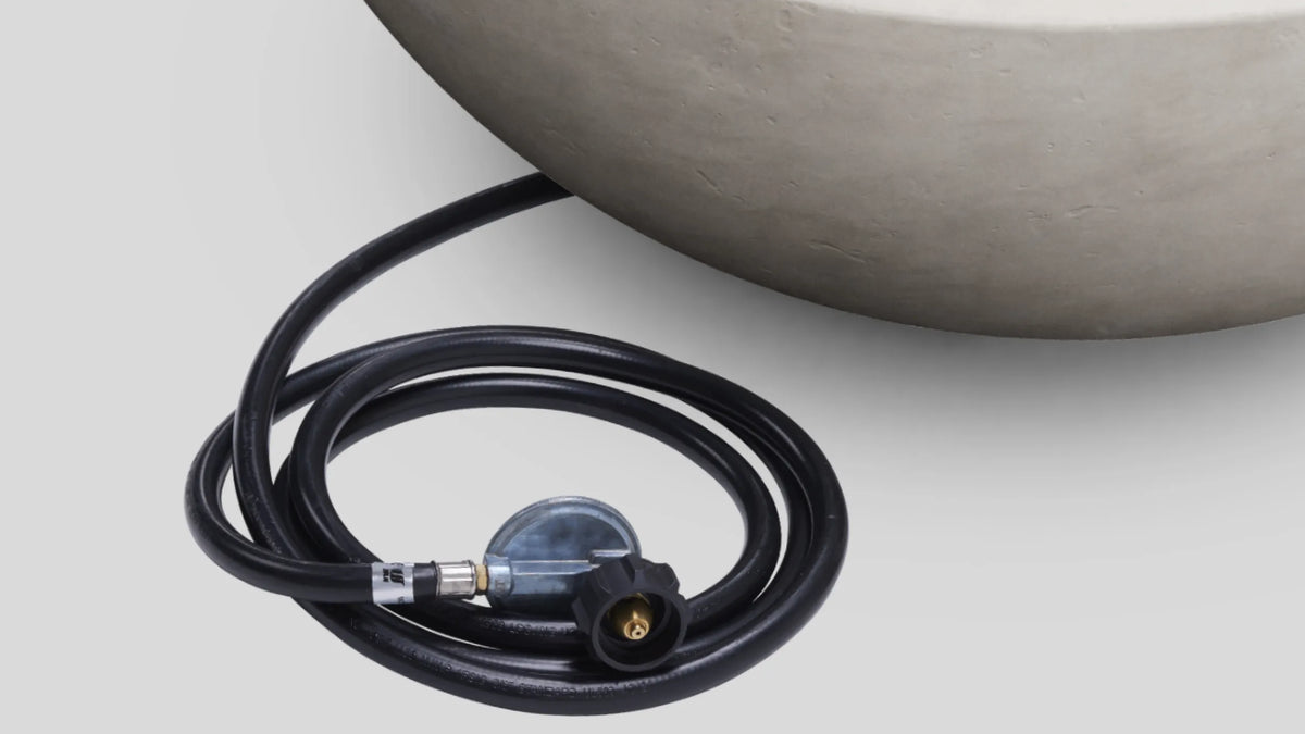 Gas connection kit — propane hose and regulator laid beside a concrete fire table bowl on white background