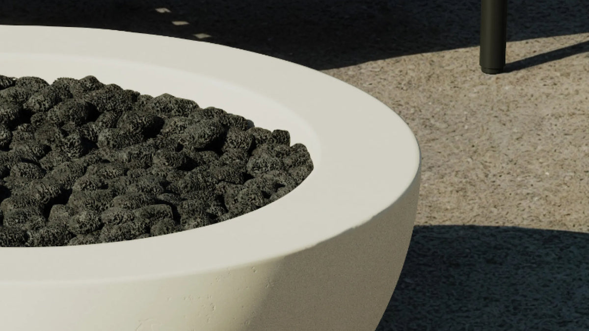 Lava rock fill detail — angled view of concrete fire table bowl filled with lava rocks on a stone patio, unlit