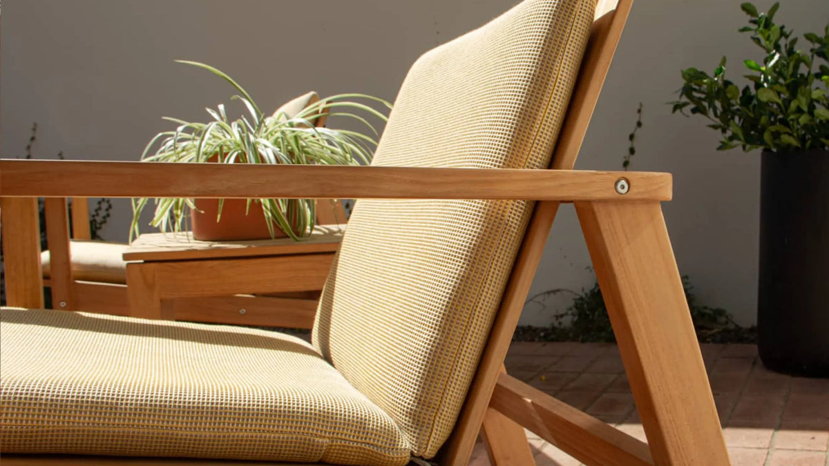 Low Lounge Chair with yellow woven grid-pattern cushions and teak frame on a terracotta tile patio, 3/4 front view