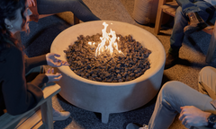 Group of people gathered around a round concrete fire table with lava rock and open flame at night — Fire Tables collection