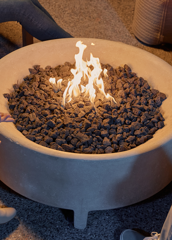 Group of people gathered around a round concrete fire table with lava rock and open flame at night — Fire Tables collection