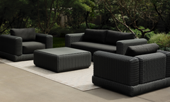 Dark charcoal all-wicker outdoor lounge set — sofa, armchair, and square coffee table on a concrete patio with garden backdrop — Wicker Outdoor Furniture collection
