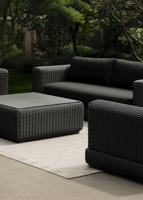 Dark charcoal all-wicker outdoor lounge set — sofa, armchair, and square coffee table on a concrete patio with garden backdrop — Wicker Outdoor Furniture collection