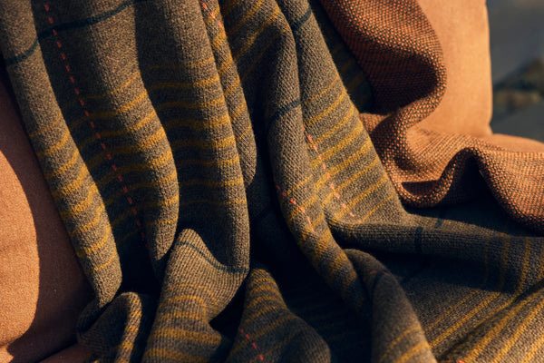 Close-up of a striped woven throw blanket draped over a terracotta outdoor sofa cushion in warm light