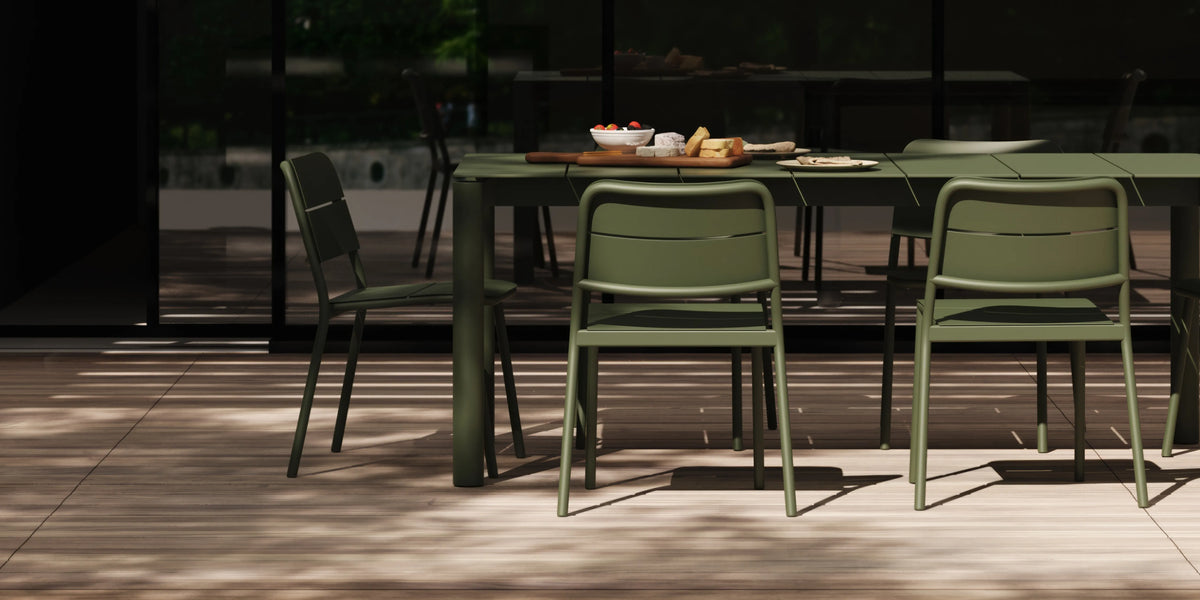 Olive green aluminum dining table and chairs on a sunlit terrace, food and tableware on the surface