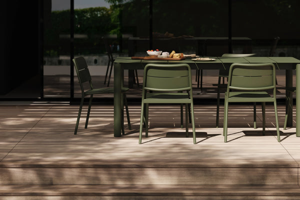 Olive green aluminum dining table and chairs on a sunlit terrace, food and tableware on the surface