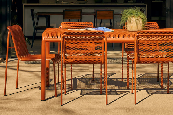 Orange perforated metal dining table and chairs on a concrete patio with a desert cactus garden