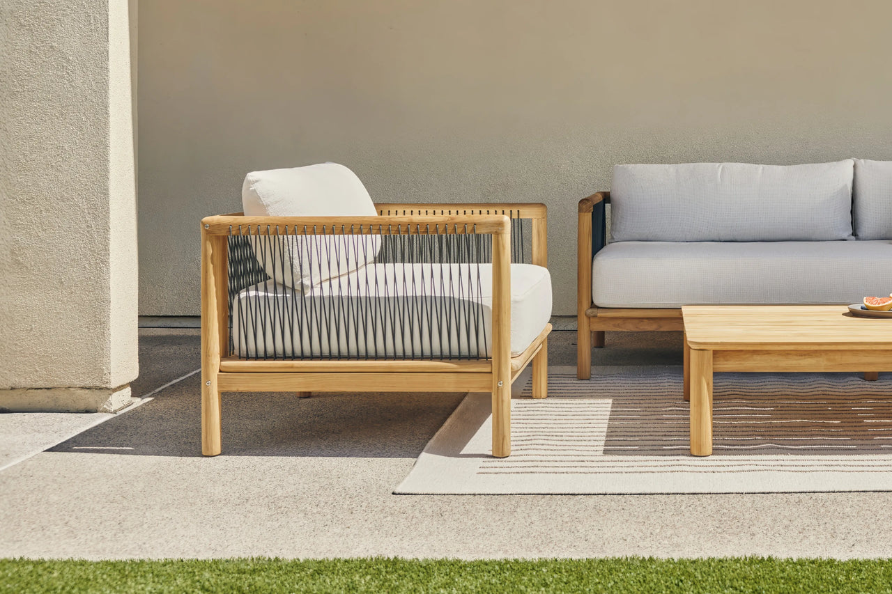 Teak lounge chair, sofa, and round side table styled on a striped outdoor rug against a stucco wall