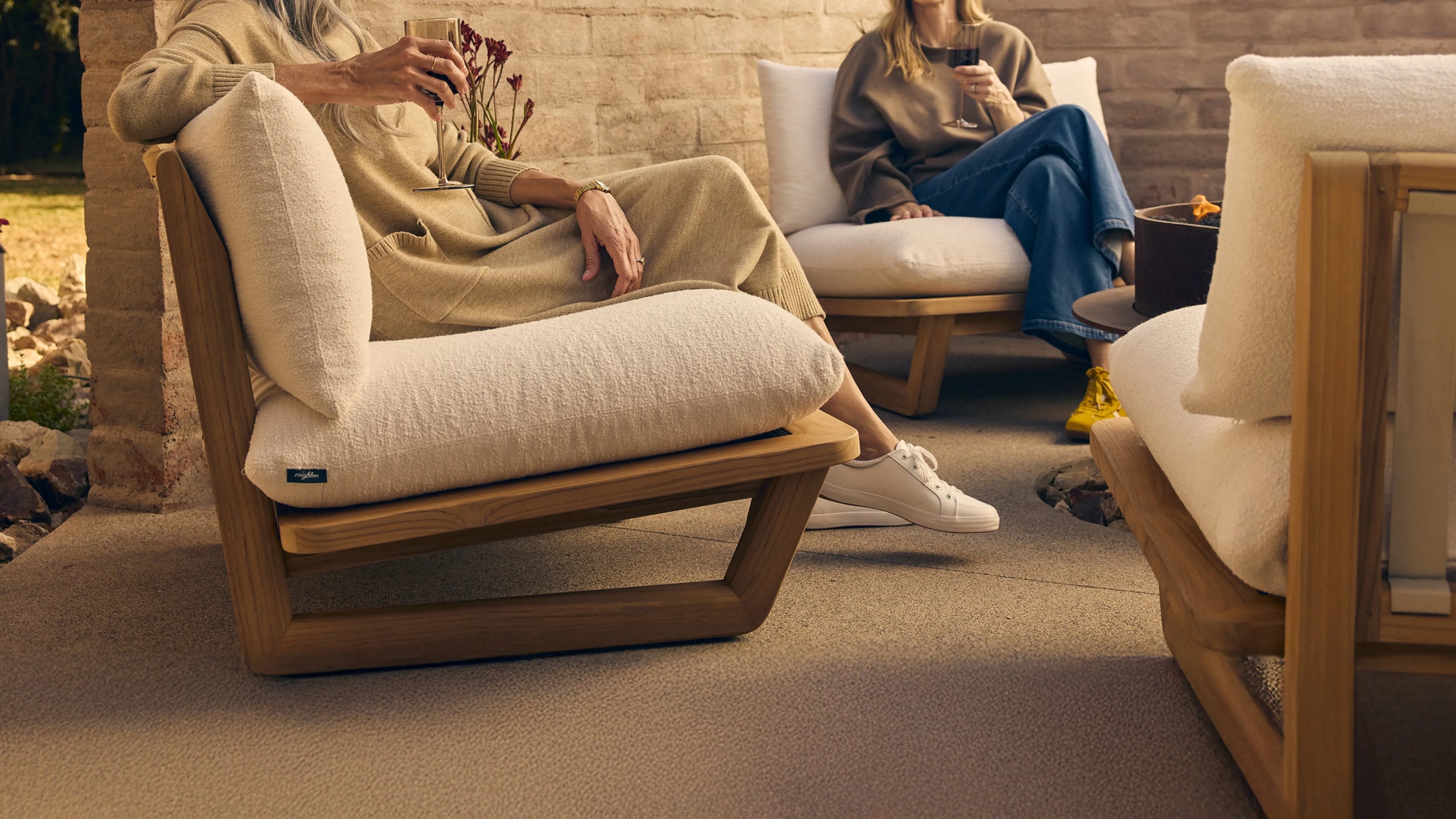 Close-up of a woman relaxing in a teak lounge chair with cream boucle cushions, holding a glass outdoors