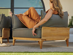 Woman relaxing in Neighbor Bluff Chair and a Half upholstered in gray fabric with wood frame, modern interior