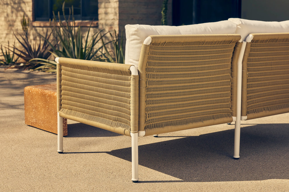 Neighbor Camber Chair with woven wicker back and cream cushion in a sunny desert courtyard with sculptural plants.